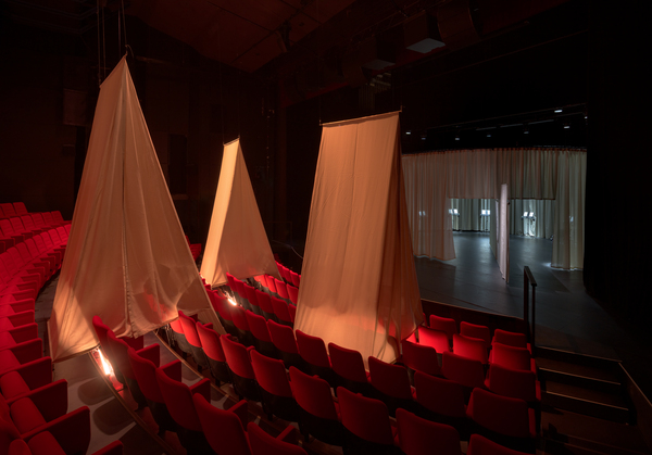 An auditorium with tent-like structures in over some of the seats and a circular curtain on the stage