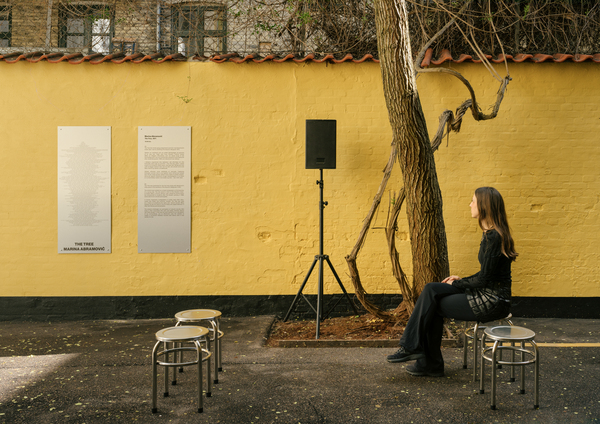 A person sat listening under a tree with a speaker and metal signage with a design and some text